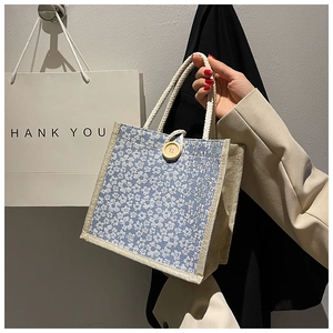 Detail of blue floral canvas tote bag featuring thick rope handles and a wooden button