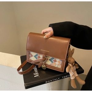 Close-up of brown leather bag with woven pattern, metal pendant and a cute rabbit doll