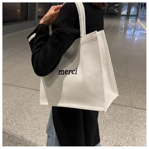 Vista laterale di una grande borsa tote in tela bianca con scritta merci nera