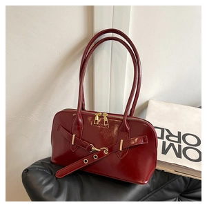 Detail of burgundy patent leather handbag with gold zippers and buckle strap