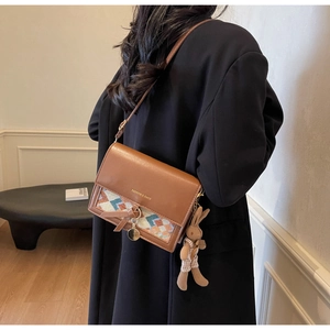 Brown crossbody bag with woven flap and rabbit charm worn over a long black coat