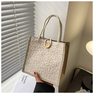 Close-up of woven linen handbag featuring white floral embroidery and a wooden button closure