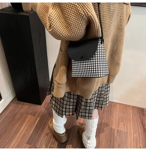 Detail of a houndstooth woven shoulder bag with black leather flap and thin strap