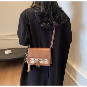 Close-up of brown leather crossbody bag with geometric weave and teddy bear charm
