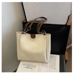 Detail of cream tote bag featuring brown handles and gold chain hardware on a chair