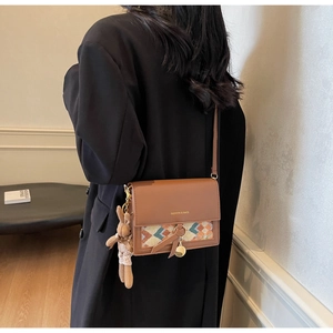 Detail of brown crossbody bag featuring woven pattern and a cute plush rabbit charm
