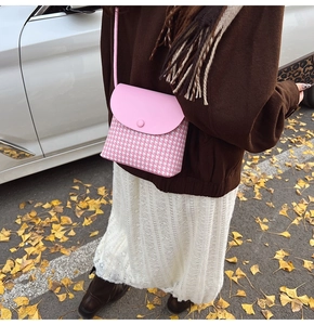 Close-up of pink houndstooth crossbody bag with round buckle and leather strap