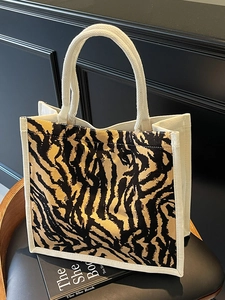 Close-up of tiger print canvas tote bag featuring woven rope handles on a black leather seat