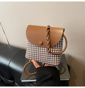 Detailed close-up of a houndstooth crossbody bag featuring a brown leather flap and woven handle