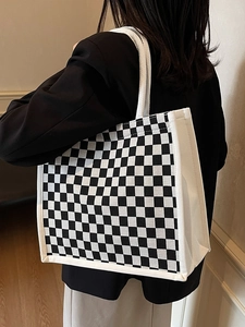 Detail of checkered canvas tote bag with wide white shoulder strap worn by a model
