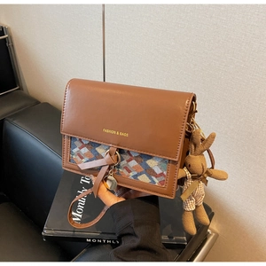 Close-up of vintage brown leather bag with plaid fabric flap and cute bunny charm