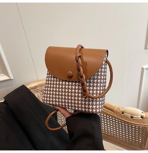 Detail of houndstooth crossbody bag featuring brown leather flap and thick woven rope strap