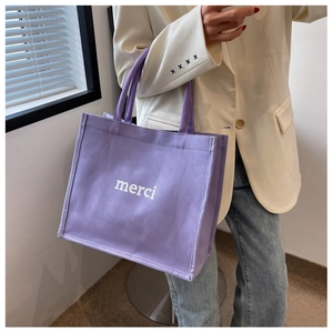 Dettaglio della borsa tote in tela viola con scritta merci portata da una modella