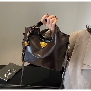 Nahaufnahme braune Lackleder-Handtasche mit goldenem Logo und dekorativem Glockenanhänger