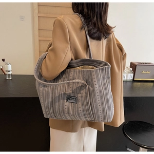 Détail du sac cabas en toile rayée grise montrant le patch logo et la texture épaisse