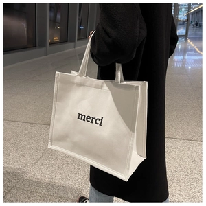 Borsa tote in tela bianca con scritta merci nera portata a tracolla