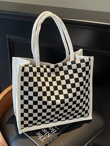 Detail of checkered canvas tote bag with reinforced handles on a black leather chair