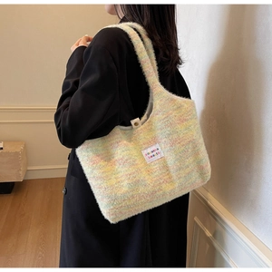 Detail of colorful knit tote bag with brand label worn on shoulder in minimalist interior