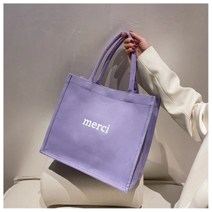 Dettaglio della borsa tote in tela lilla con scritta merci tenuta da una modella