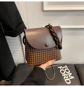 Detail of vintage houndstooth handbag with woven handle and dark brown leather flap
