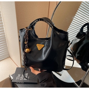 Detailansicht der schwarzen Ledertasche mit goldenem Dreieckslogo und Glockenanhänger