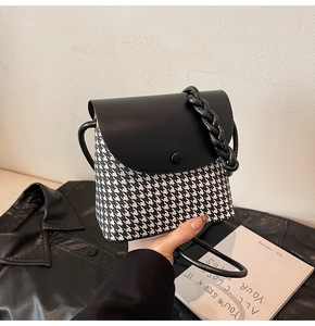 Detail of houndstooth crossbody bag with black leather flap and woven handle