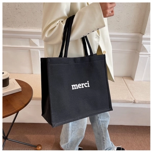 Dettaglio della borsa tote in tela nera con scritta merci bianca e manici resistenti