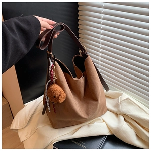 Detail view of brown faux suede bucket bag with teddy bear charm and plaid ribbon