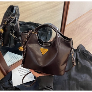 Details einer braunen Vintage-Lederhandtasche mit Metalldreieck-Logo und Deko-Anhängern
