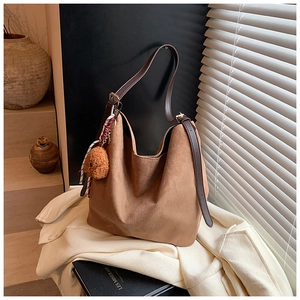 Gros plan du sac hobo en daim marron avec bandoulière en cuir et charm chien en peluche