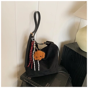Détail du cabas en daim noir avec corde tressée et pendentif ours en peluche sur livres