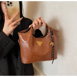 Detail einer braunen Leder-Tragetasche mit goldenem Dreieckslogo und Glockenanhänger