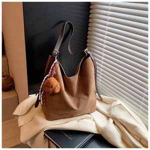 Gros plan d'un cabas en daim marron avec breloque chiot et ruban sur manteau