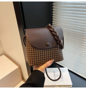 Detail of a brown leather and houndstooth crossbody bucket bag with woven handle