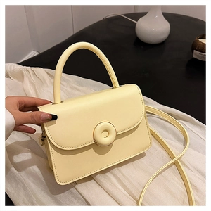 Detail of light yellow crossbody bag featuring a round buckle on the front flap