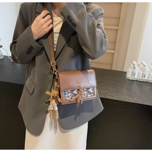 Detail of a brown leather crossbody bag with geometric woven flap and bunny charm