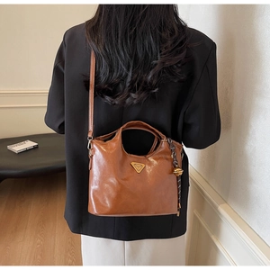 Detailansicht einer braunen Vintage-Ledertasche mit Goldlogo und schickem Anhänger