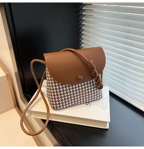 Detail of houndstooth patterned crossbody bag with brown leather flap on a book