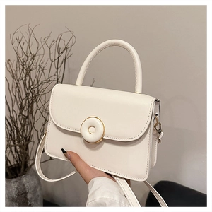 Detail of minimalist beige crossbody bag featuring round metal buckle and top handle