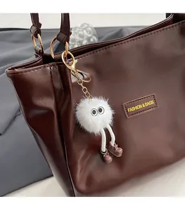Detail of dark brown faux leather tote bag with monster plush charm and logo