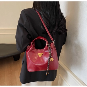 Detail der weinroten glänzenden Lederhandtasche mit goldenem Logo und gewebtem Anhänger