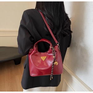 Detail der dunkelroten Vintage-Handtasche mit goldenem Logo und Seilanhänger an einem Model