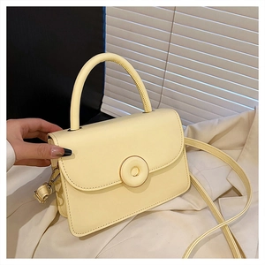 Detail of a creamy yellow crossbody bag with a round buckle on a white background