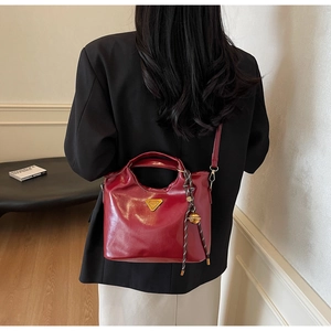 Detail der burgunderroten Lackledertasche mit goldenem Logo und geflochtenem Anhänger