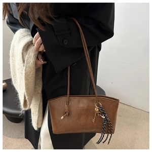 Close-up of brown leather tote bag detail with metal key pendant and stylish silk ribbon