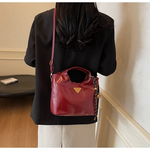 Detail der dunkelroten Lacklederhandtasche mit Goldlogo und dekorativem Riemengriff