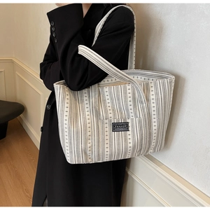 Détail d'un grand sac cabas rayé porté avec un manteau long en laine noir élégant