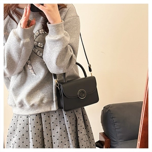 Model wearing a black rectangular crossbody bag with a circular twist lock and top handle