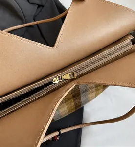 Detail of smooth gold metal zipper and stitching on plaid fabric shoulder bag