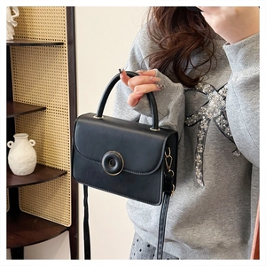 Detail of black matte faux leather crossbody bag with a circular gold decorative buckle